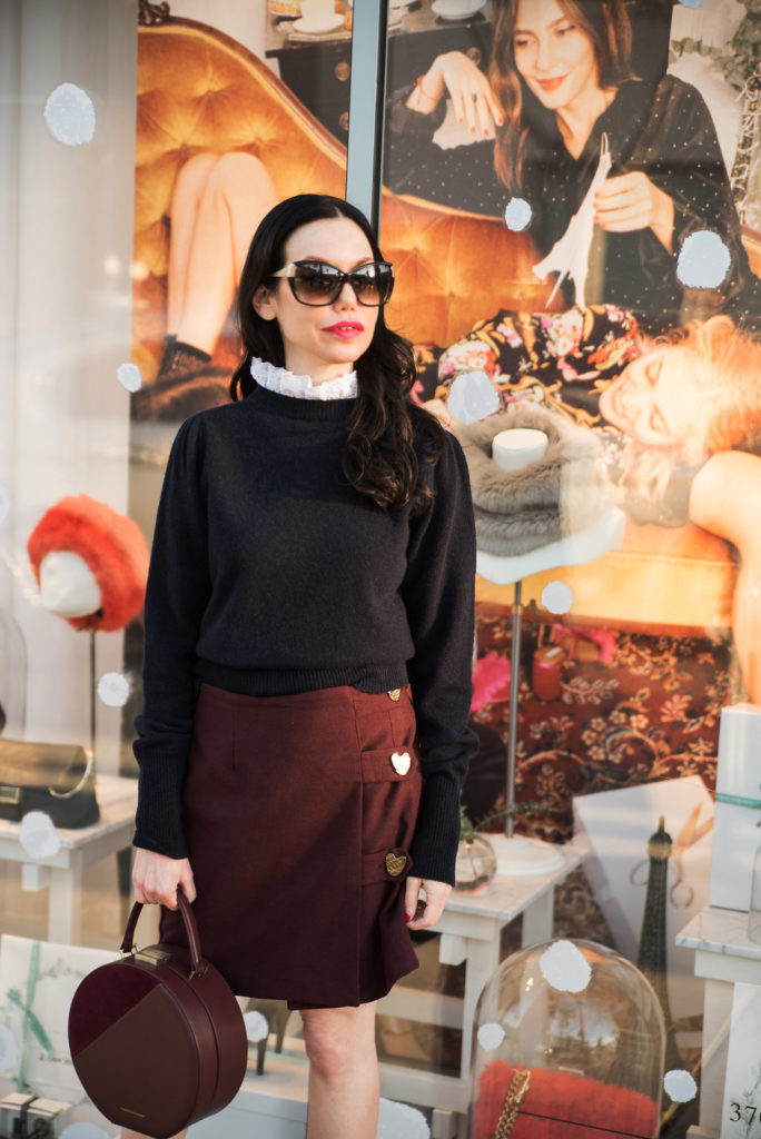 How to Dress Like a Parisian Girl, styling tips featured by top LA fashion blog, Pretty Little Shoppers: image of a woman wearing a Sandro sweater, Storets mini skirt, Tammy & Benjamin bag, Tommy Hilfiger ankle boots, and Oliver Peoples sunglasses.