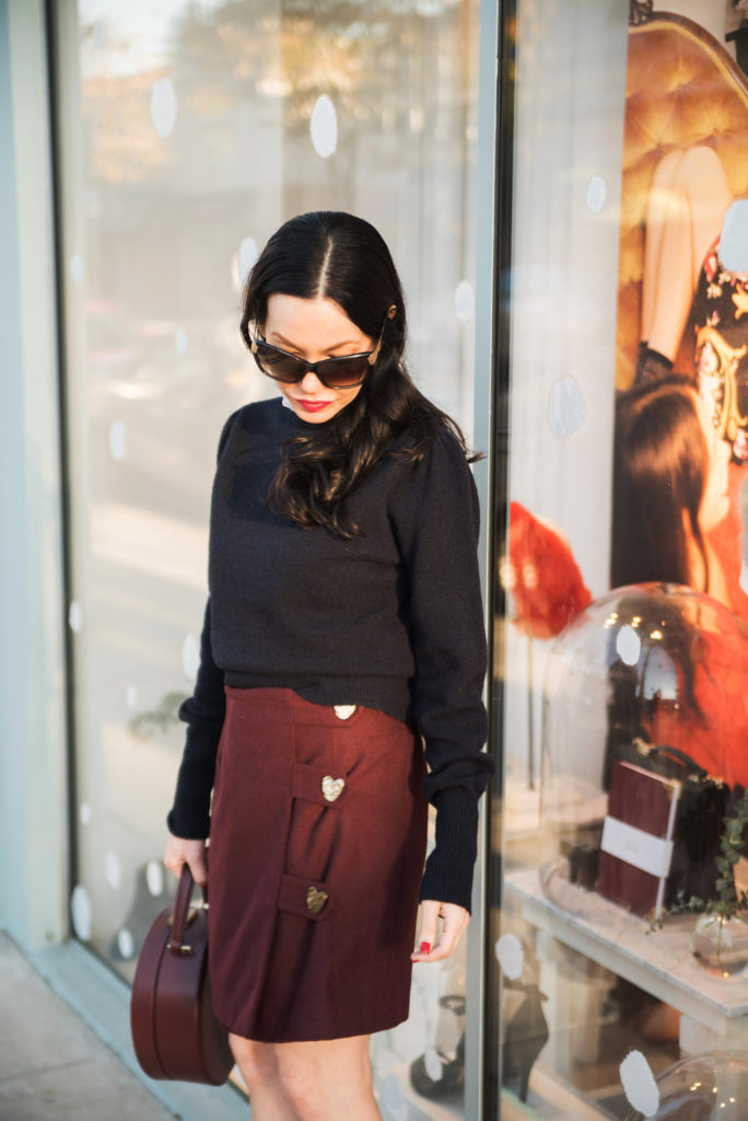 How to Dress Like a Parisian Girl, styling tips featured by top LA fashion blog, Pretty Little Shoppers: image of a woman wearing a Sandro sweater, Storets mini skirt, Tammy & Benjamin bag, Tommy Hilfiger ankle boots, and Oliver Peoples sunglasses.