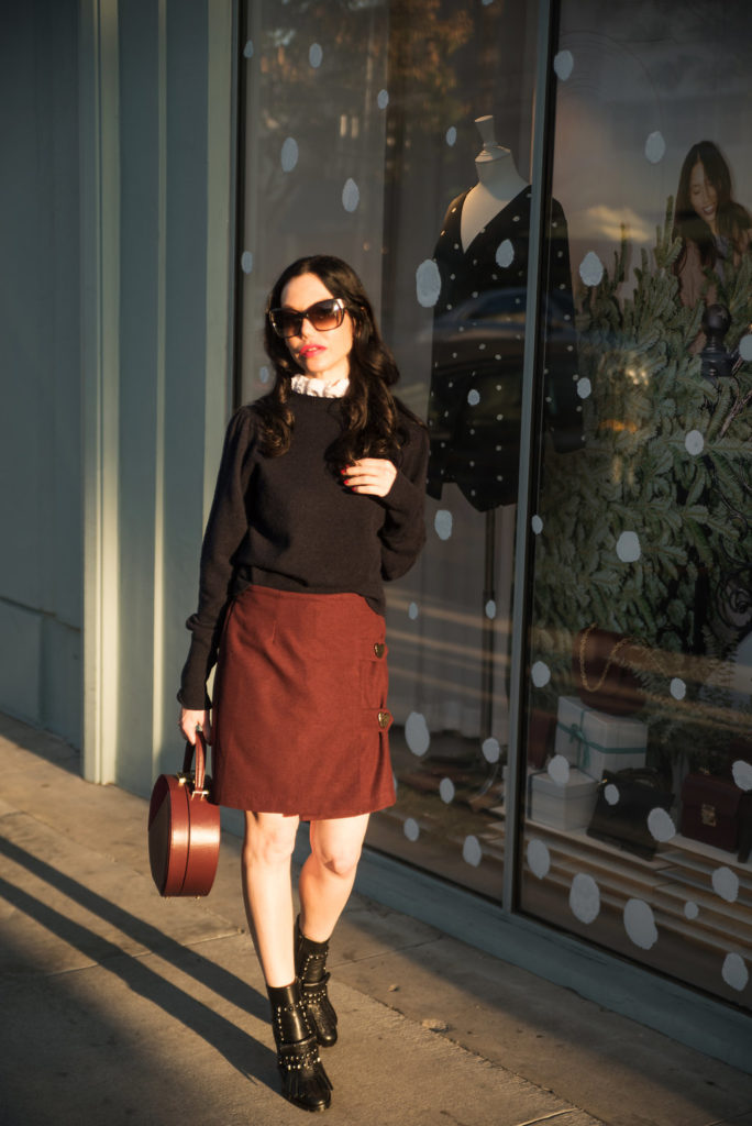 How to Dress Like a Parisian Girl, styling tips featured by top LA fashion blog, Pretty Little Shoppers: image of a woman wearing a Sandro sweater, Storets mini skirt, Tammy & Benjamin bag, Tommy Hilfiger ankle boots, and Oliver Peoples sunglasses.