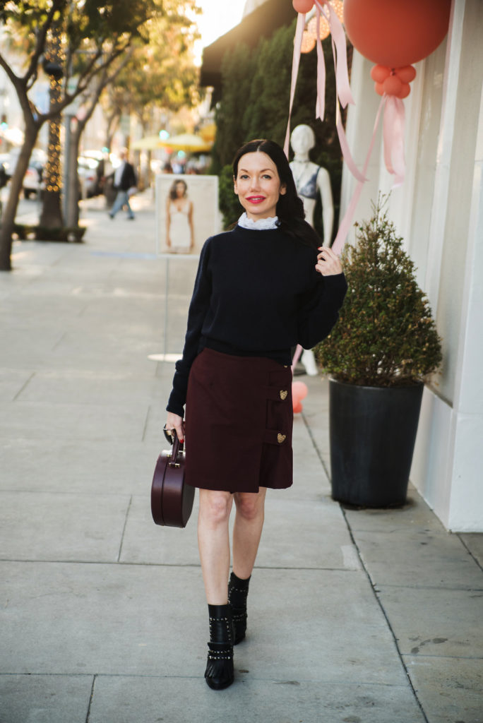 How to Dress Like a Parisian Girl, styling tips featured by top LA fashion blog, Pretty Little Shoppers: image of a woman wearing a Sandro sweater, Storets mini skirt, Tammy & Benjamin bag, Tommy Hilfiger ankle boots, and Oliver Peoples sunglasses.