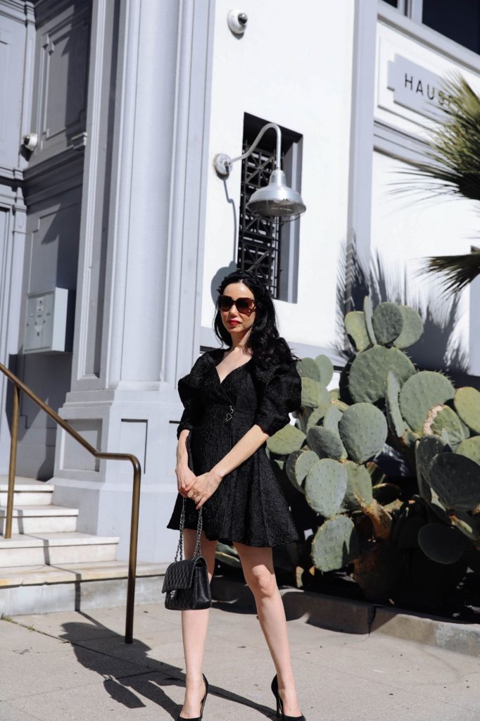 Sister Jane, Little Black Dress, Gucci Sunglasses, Spring Style, What to wear in the Spring, Seasonal Style, What to wear, Ladylike style, Los Angeles Fashion Blogger, Personal Style, Outfit Inspiration, OOTD Inspo, street style stalking, Preppy Style, Parisian Chic, Classic and Feminine, How to style a little black dress #dreamsisterjane #Springstyle #ootd #sisterjane | Sister Jane by popular LA fashion blog, Pretty Little Shoppers: image of a woman standing outside an wearing a Sister Jane black puff sleeve dress, Neiman Marcus pumps, Tarina Tarantino headband, Gucci 58MM Oversized Square Sunglasses, and holding a CHANEL PRE-OWNED Double Flap quilted shoulder bag. 