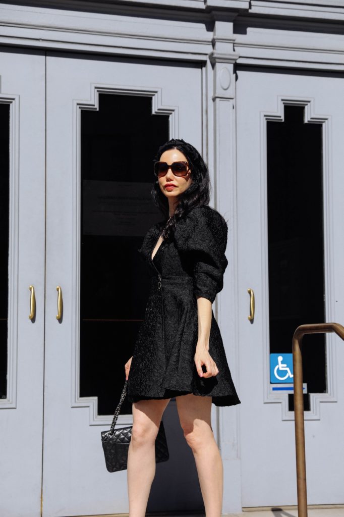 Sister Jane, Little Black Dress, Gucci Sunglasses, Spring Style, What to wear in the Spring, Seasonal Style, What to wear, Ladylike style, Los Angeles Fashion Blogger, Personal Style, Outfit Inspiration, OOTD Inspo, street style stalking, Preppy Style, Parisian Chic, Classic and Feminine, How to style a little black dress #dreamsisterjane #Springstyle #ootd #sisterjane | Sister Jane by popular LA fashion blog, Pretty Little Shoppers: image of a woman standing outside an wearing a Sister Jane black puff sleeve dress, Neiman Marcus pumps, Tarina Tarantino headband, Gucci 58MM Oversized Square Sunglasses, and holding a CHANEL PRE-OWNED Double Flap quilted shoulder bag. 