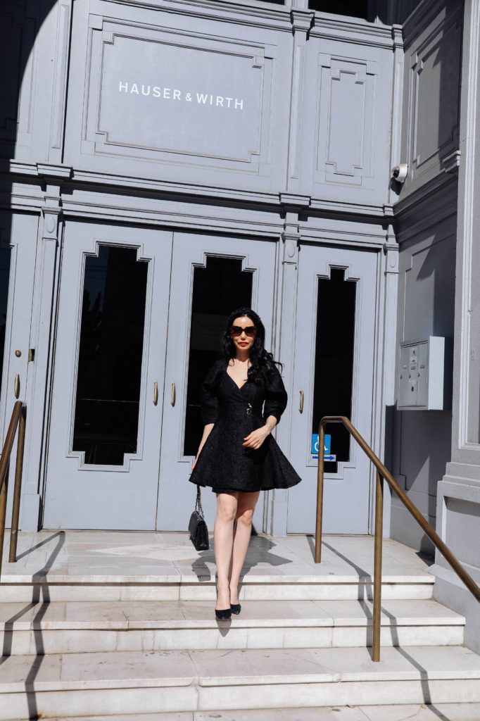 Sister Jane, Little Black Dress, Gucci Sunglasses, Spring Style, What to wear in the Spring, Seasonal Style, What to wear, Ladylike style, Los Angeles Fashion Blogger, Personal Style, Outfit Inspiration, OOTD Inspo, street style stalking, Preppy Style, Parisian Chic, Classic and Feminine, How to style a little black dress #dreamsisterjane #Springstyle #ootd #sisterjane | Sister Jane by popular LA fashion blog, Pretty Little Shoppers: image of a woman standing outside an wearing a Sister Jane black puff sleeve dress, Neiman Marcus pumps, Tarina Tarantino headband, Gucci 58MM Oversized Square Sunglasses, and holding a CHANEL PRE-OWNED Double Flap quilted shoulder bag. 