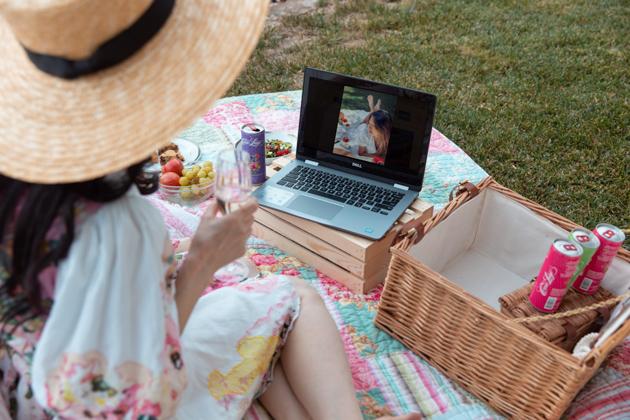 How to Host A Virtual Picnic, Quarantine Life, Things to do during Quarantine Outside, Virtual Picnic Menu, Things to do in your backyard #VirtualPicnic #SummerPicnic #QuarantineActivities | Virtual Picnic by popular L.A. lifestyle blog, Pretty Little Shoppers: image of a woman wearing a Teien Mini Dress HEMANT AND NANDITA brand: HEMANT AND NANDITA and Amazon Lack of Color Women's The Spencer Boater Hat and sitting next to a wicker picnic basket, wooden crates, plates of food, and some Casa Luigi sparkling wine on a patchwork quilt outside. 