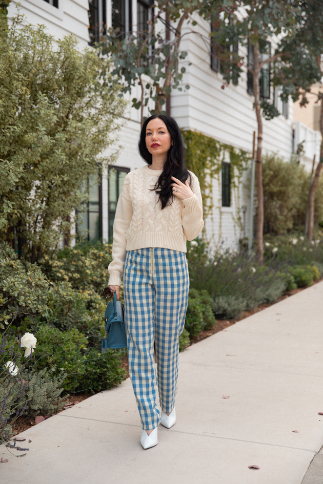 How to Wear Gingham for Fall, What to wear Fall 2020, Fall Transitional Look, Capulet Gingham Pants, White Cable knit Sweater, Joseph and Stacey Bag, Los Angeles Fashion Blogger, Pretty Little Shoppers Blog #Gingham #GinghamStyle | Fall Clothing by popular L.A. fashion blog, Pretty Little Shoppers: image of a woman walking down a sidewalk and wearing a pair of Capulet gingham pants, J.O.A sweater, Aqua mules and carrying a Joseph and Stacey bag.  