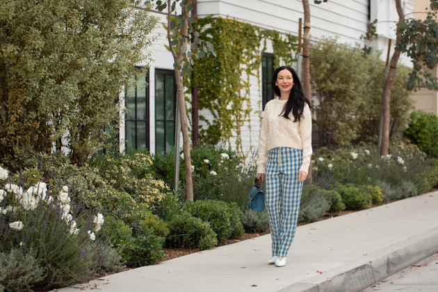 How to Wear Gingham for Fall, What to wear Fall 2020, Fall Transitional Look, Capulet Gingham Pants, White Cable knit Sweater, Joseph and Stacey Bag, Los Angeles Fashion Blogger, Pretty Little Shoppers Blog #Gingham #GinghamStyle | Fall Clothing by popular L.A. fashion blog, Pretty Little Shoppers: image of a woman walking down a sidewalk and wearing a pair of Capulet gingham pants, J.O.A sweater, Aqua mules and carrying a Joseph and Stacey bag.  