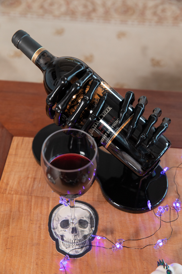 Skeleton Hands Wine Holder |Cheese Platter by popular LA lifestyle blog, Pretty Little Shoppers: image of a glass of red wine next to a bottle of red wine in a black skeleton hands wine holder. 