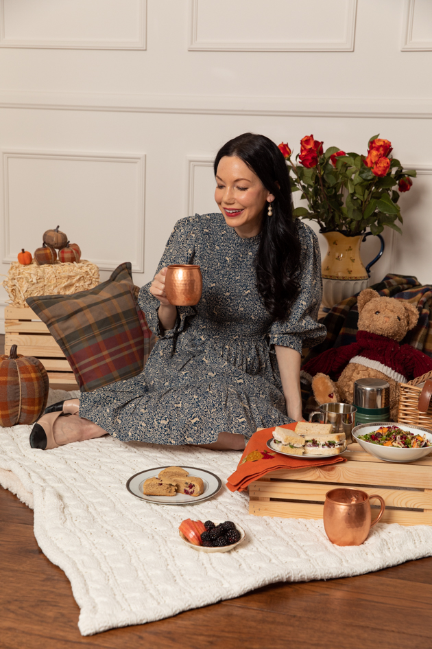 Indoor Fall Picnic, Fall Harvest Picnic Menu, Doen Fawn Dress, Lisa Valerie Morgan, Pretty Little Shoppers Blog, Los Angeles Lifestyle Blogger, How to Celebrate Thanksgiving During Quarantine, Holiday Ideas During Covid Quarantine #IndoorPicnic #ThanksgivingIdeas |Fall Picnic by popular LA lifestyle blog, Pretty Little Shoppers: image of a woman sitting on a knit cream blanket and having an indoor picnic. 