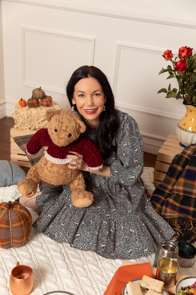 Indoor Fall Picnic, Fall Harvest Picnic Menu, Doen Fawn Dress, Lisa Valerie Morgan, Pretty Little Shoppers Blog, Los Angeles Lifestyle Blogger, How to Celebrate Thanksgiving During Quarantine, Holiday Ideas During Covid Quarantine #IndoorPicnic #ThanksgivingIdeas |Fall Picnic by popular LA lifestyle blog, Pretty Little Shoppers: image of a woman sitting on a knit cream blanket and holding a stuffed bear.