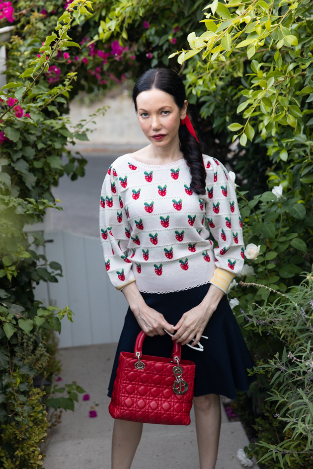 Fall Transitional Look, Waiting for Election Results, Red White and Blue Outfit, LoveShackFancy Strawberry Sweater, Tommy Hilfiger Collection Skirt, Italic Cateye Sunglasses, Lady Dior Bag, Classic and Feminine Style, What to Wear for Fall, Fall in Los Angeles, Preppy Style Los Angeles Lifestyle Blogger, Pretty Little Shoppers Blog #FallTransitionalLook #PreppyStyle | Fall Clothing by popular L.A. fashion blog, Pretty Little Shoppers: image of a woman wearing a strawberry Net-A-Porter sweater, Dior purse, Tommy Hilfiger skirt, plaid block heel sandals, and Italic sunglasses.