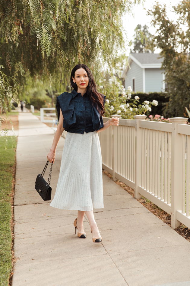 By Abigal Love blue Statement blouse with Black quilted Chanel bag | Life Update by popular LA lifestyle blog, Pretty Little Shoppers: image of a woman wearing a By Abigal Love blue Statement blouse, grey pleated skirt and carrying a Black quilted Chanel bag 