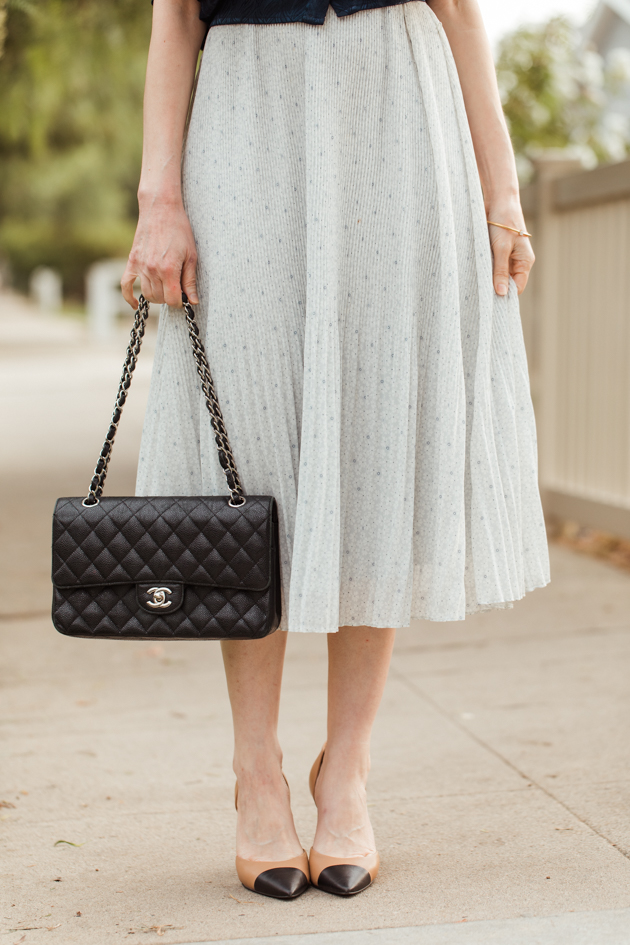 Abercrombie and Fitch pleated dress with black Chanel bag and cap toe pumps |Life Update by popular LA lifestyle blog, Pretty Little Shoppers: image of a woman standing next to a white picket fence and wearing a By Abigal Love blue Statement blouse, grey pleated skirt and carrying a Black quilted Chanel bag.