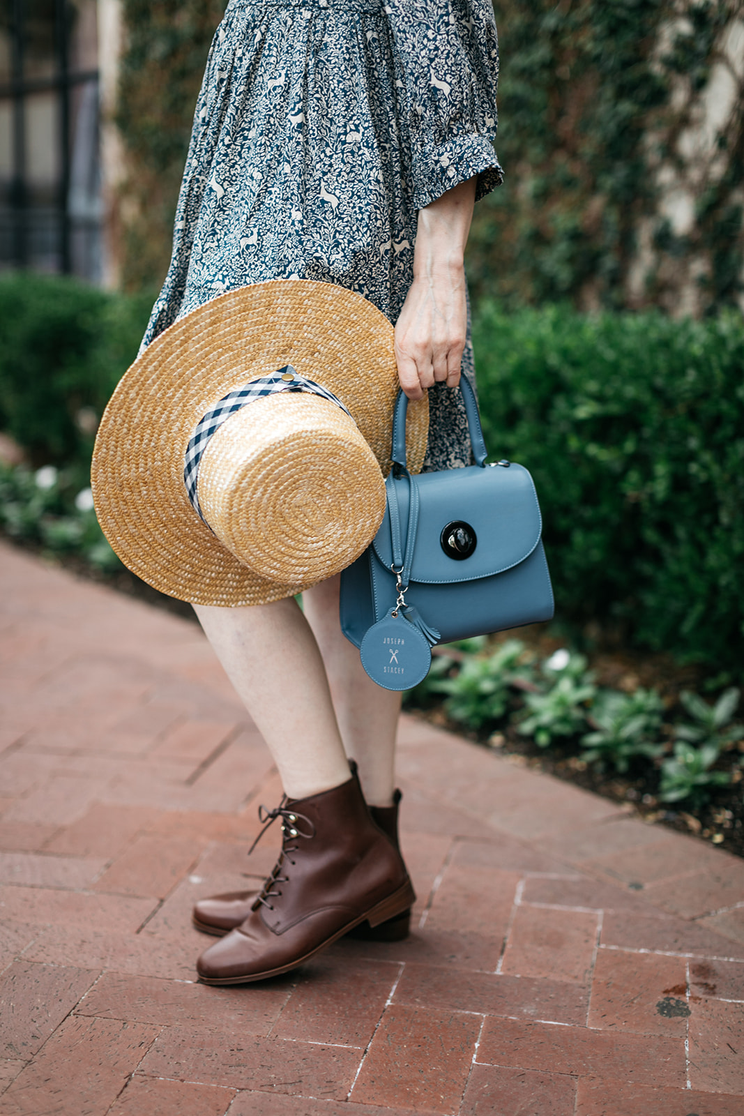 Cottagecore Style, Lack of Color Boater Hat with Sezane Booties and Joseph and Stacey Dress.   Romantic Dress by popular Dallas fashion blog, Pretty Little Shoppers: image of a woman walking on a brick pathway next to a building covered in ivy and wearing a Doen Leda fawn dress, Lack of Color straw boater hat, and Suzanne booties.