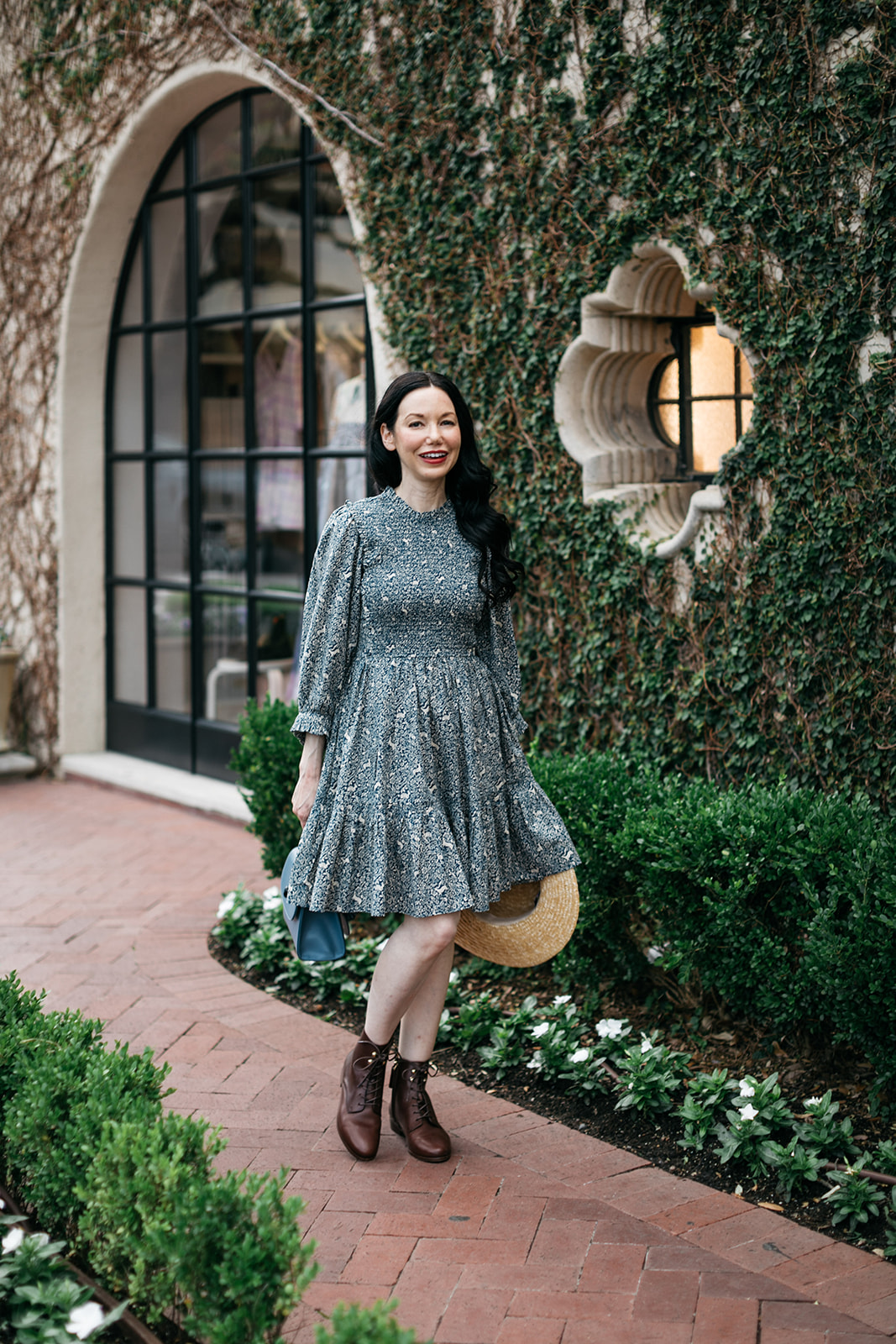 Cottagecore, Romantic Dress, Booties, Boater Hat |  Romantic Dress by popular Dallas fashion blog, Pretty Little Shoppers: image of a woman walking on a brick pathway next to a building covered in ivy and wearing a Doen Leda fawn dress, Lack of Color straw boater hat, and Suzanne booties.