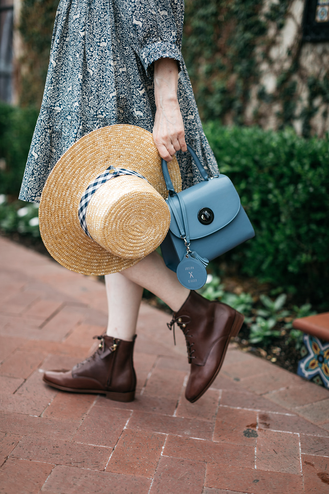 Lack of Color Boater Hat, Joseph and Stacey Bag, Sezane Booties |  Romantic Dress by popular Dallas fashion blog, Pretty Little Shoppers: image of a woman walking on a brick pathway next to a building covered in ivy and wearing a Doen Leda fawn dress, Lack of Color straw boater hat, and Suzanne booties.