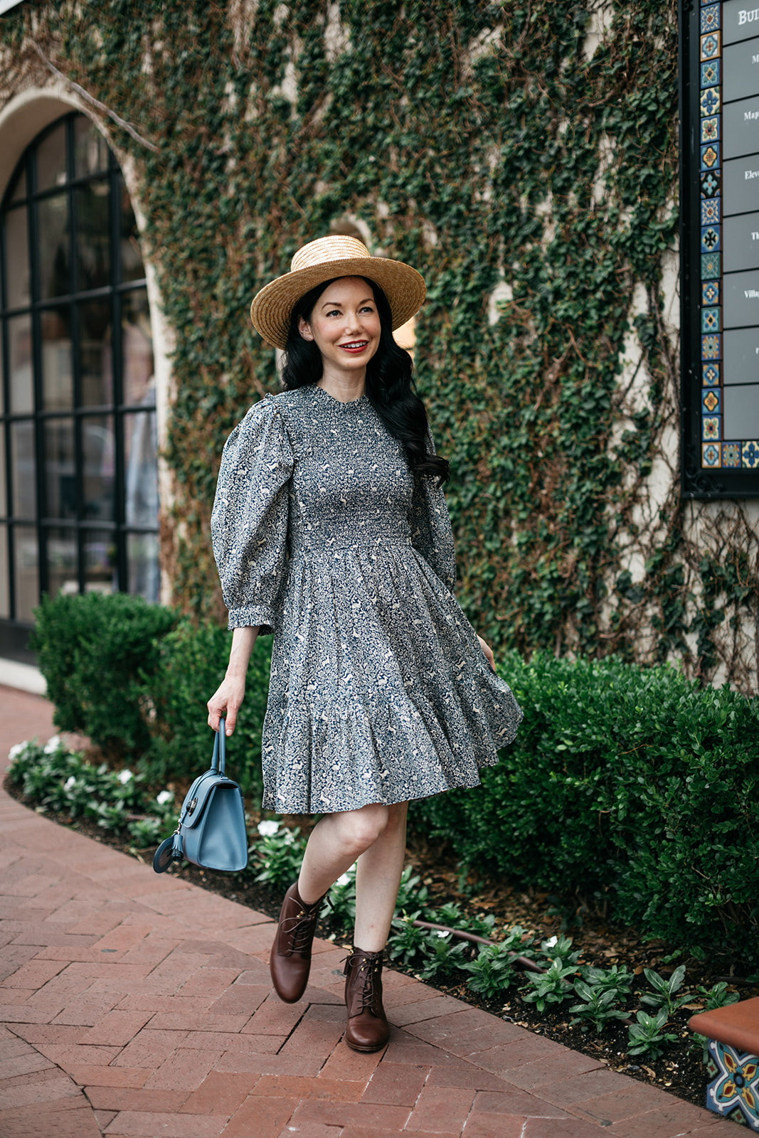 Cottagecore, Romantic Dress, Sezane Ankle Boots |  Romantic Dress by popular Dallas fashion blog, Pretty Little Shoppers: image of a woman walking on a brick pathway next to a building covered in ivy and wearing a Doen Leda fawn dress, Lack of Color straw boater hat, and Suzanne booties.