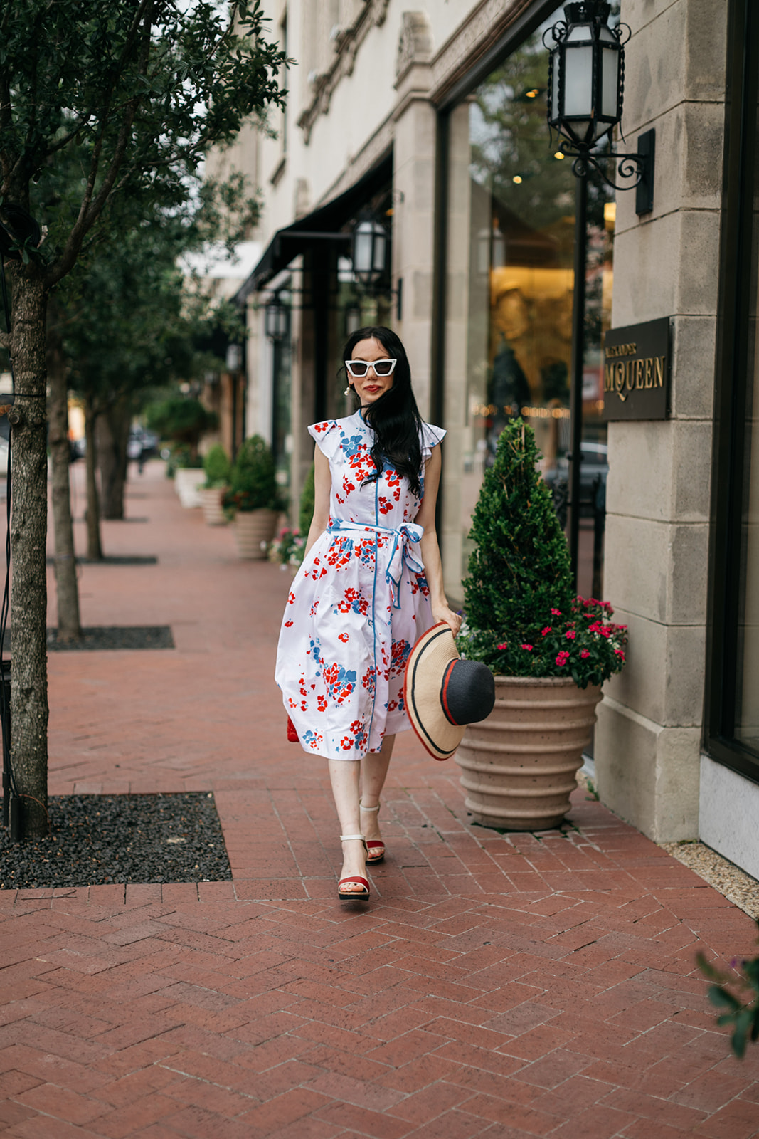 Brooks Brothers Shirt Dress, Highland Park Village | Brooks Brothers Shirt Dress by popular Dallas fashion blog, Pretty Little Shoppers: image of a woman walking in  Highland Park Village and wearing a red, whites and blue Brooks Brothers shirt dress, white frame sunglasses, and holding a red and black stripe straw hat. 