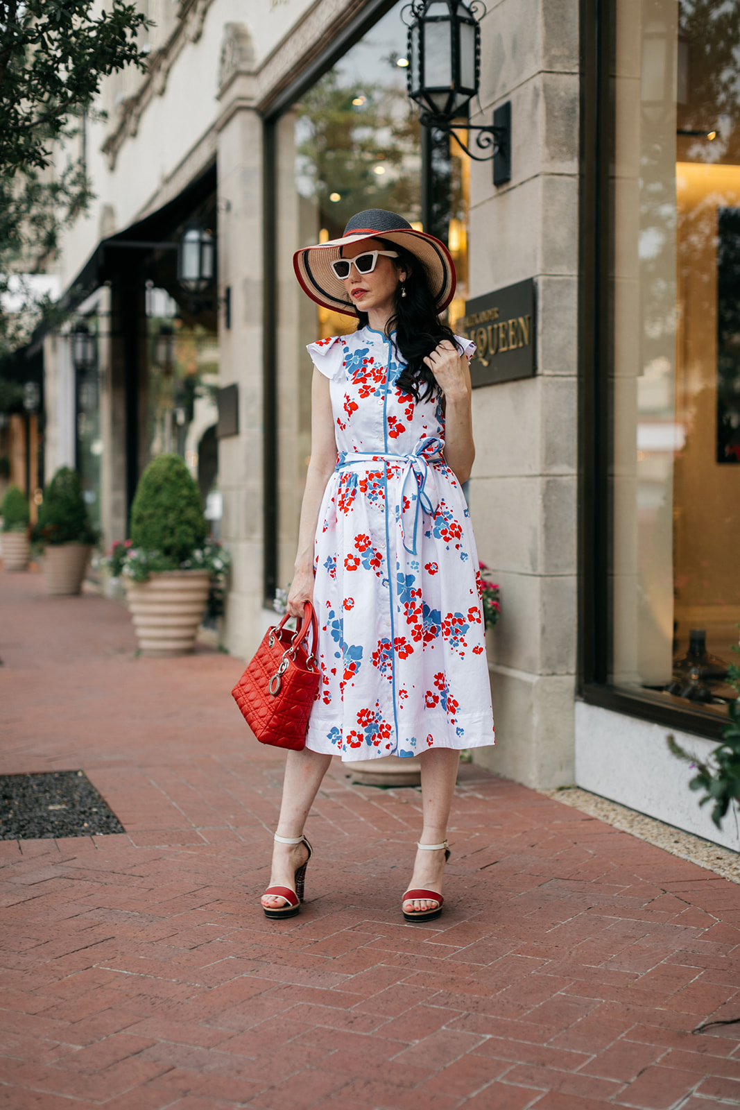 Brooks Brothers Shirt Dress, Tommy Hilfiger Sunhat and Sandals, Lady Dior Bag, Dallas Fashion Blogger | Brooks Brothers Shirt Dress by popular Dallas fashion blog, Pretty Little Shoppers: image of a woman walking in  Highland Park Village and wearing a red, whites and blue Brooks Brothers shirt dress, white frame sunglasses, and wearing a red and black stripe straw hat while holding a red handbag. 
