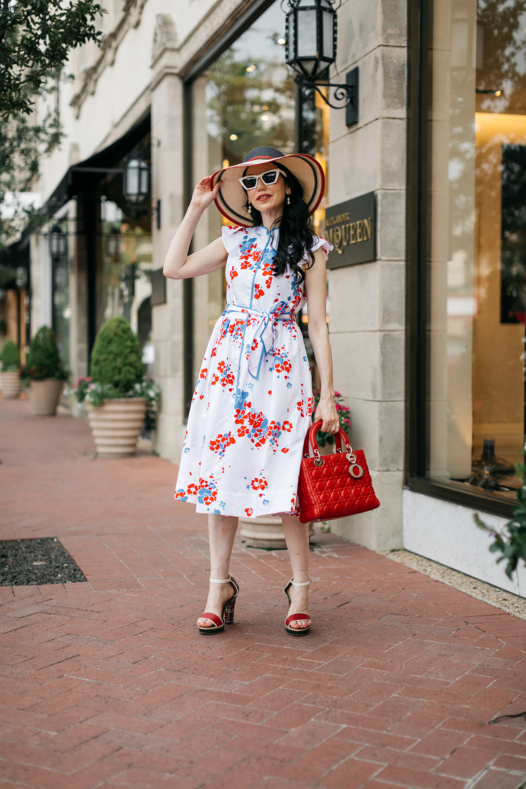 Brooks Brothers Shirt Dress, Tommy Hilfiger Sunhat and Sandals, Lady Dior Bag, Dallas Fashion Blogger |  Brooks Brothers Shirt Dress by popular Dallas fashion blog, Pretty Little Shoppers: image of a woman walking in  Highland Park Village and wearing a red, whites and blue Brooks Brothers shirt dress, white frame sunglasses, and wearing a red and black stripe straw hat while holding a red handbag. 