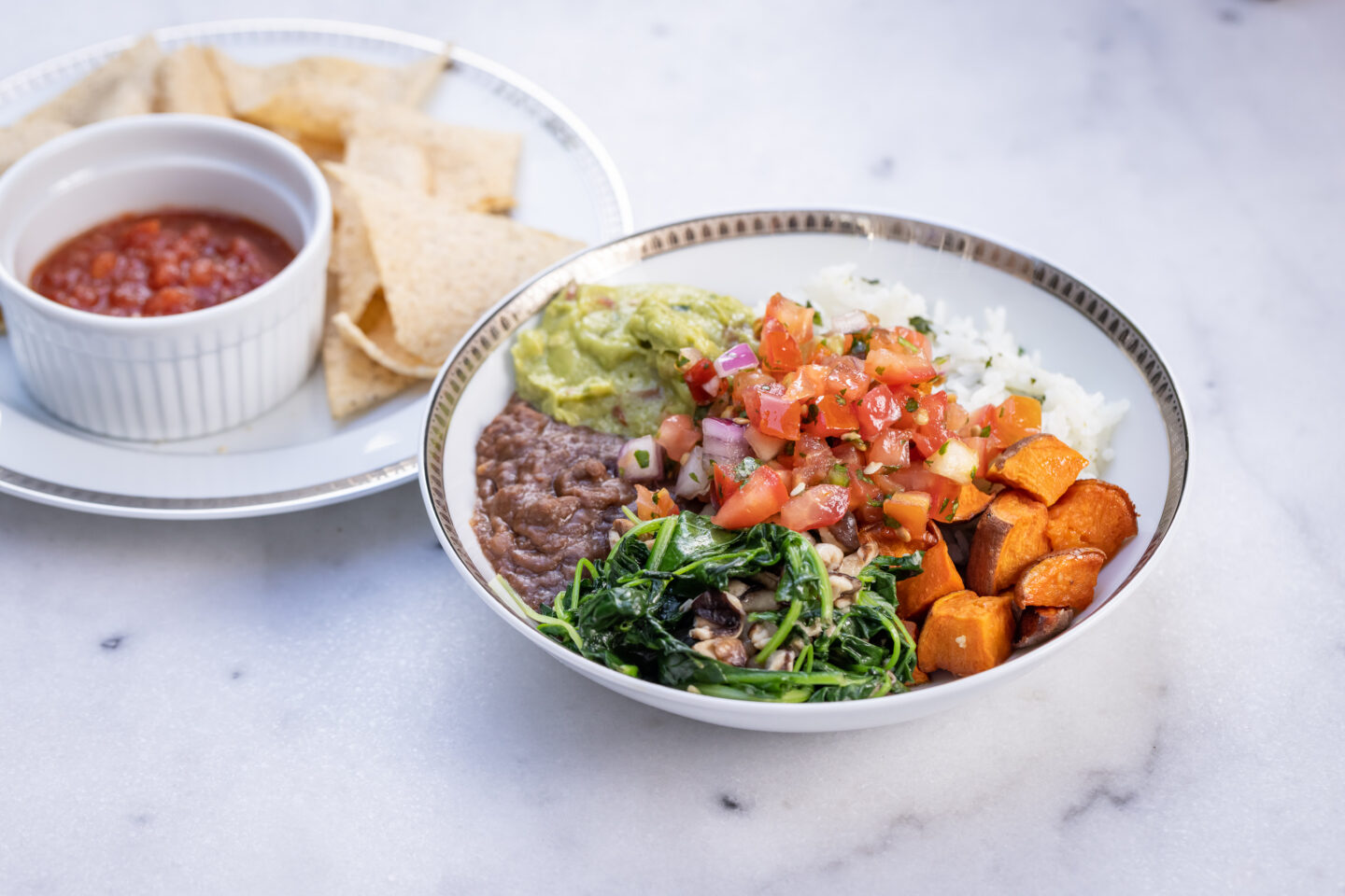 Sweet Potato, Black Bean and Cilantro Lime Rice Burrito Bowl with Sauteed Greens and Mushrooms, Pico de Gallo and Guacamole served with Siete Grain Free Chips and Salsa, Healthy Recipes, Vegan Recipes, Mexican Buddha Bowl, Gluten Free Recipes | Burrito Bowl by popular Dallas lifestyle blog, Pretty Little Shoppers: image of a sweet potato, black bean and cilantro lime rice burrito bowl next to a plate of chips and salsa. 