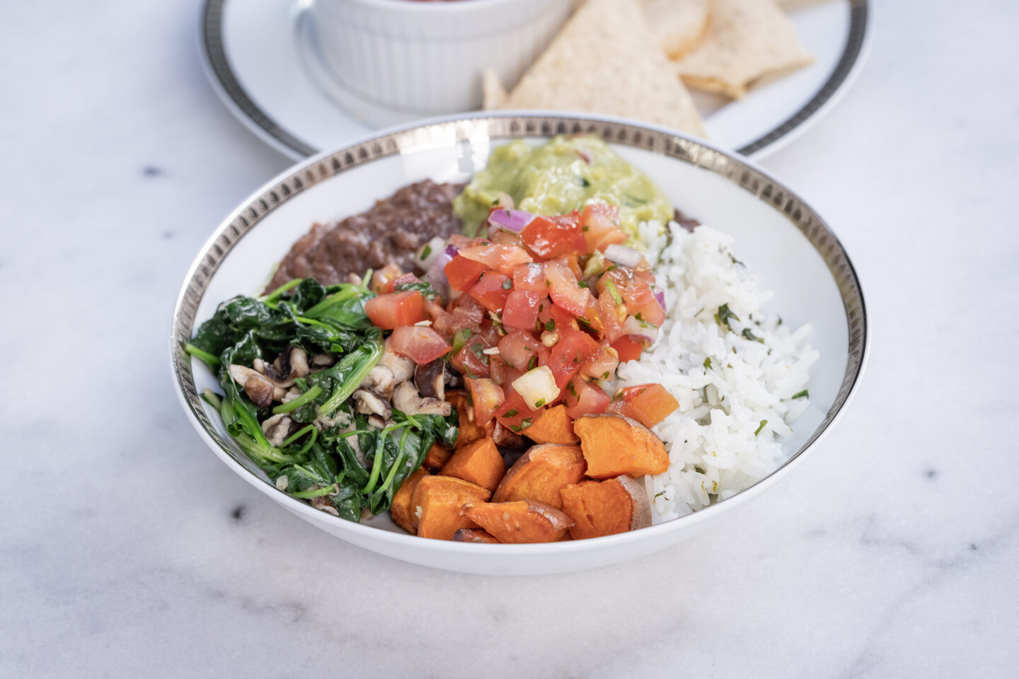 Sweet Potato, Black Bean and Cilantro Lime Rice Burrito Bowl with Sauteed Greens and Mushrooms, Pico de Gallo and Guacamole served with Siete Grain Free Chips and Salsa, Healthy Recipes, Vegan Recipes, Mexican Buddha Bowl, Gluten Free Recipes | Burrito Bowl by popular Dallas lifestyle blog, Pretty Little Shoppers: image of a sweet potato, black bean and cilantro lime rice burrito bowl next to a plate of chips and salsa. 