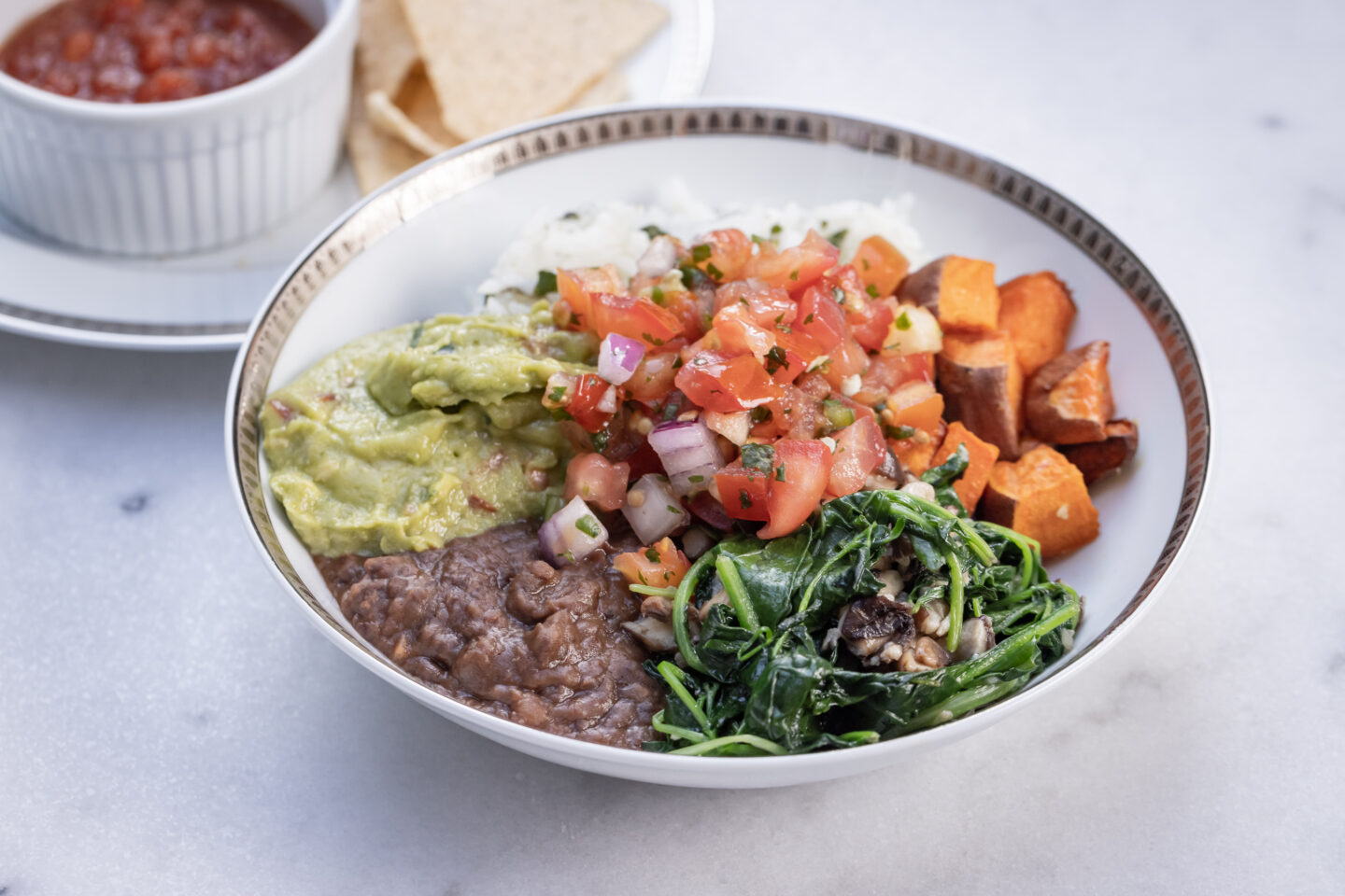 Sweet Potato, Black Bean and Cilantro Lime Rice Burrito Bowl with Sauteed Greens and Mushrooms, Pico de Gallo and Guacamole served with Siete Grain Free Chips and Salsa, Healthy Recipes, Vegan Recipes, Mexican Buddha Bowl, Gluten Free Recipes | Burrito Bowl by popular Dallas lifestyle blog, Pretty Little Shoppers: image of a sweet potato, black bean and cilantro lime rice burrito bowl next to a plate of chips and salsa. 