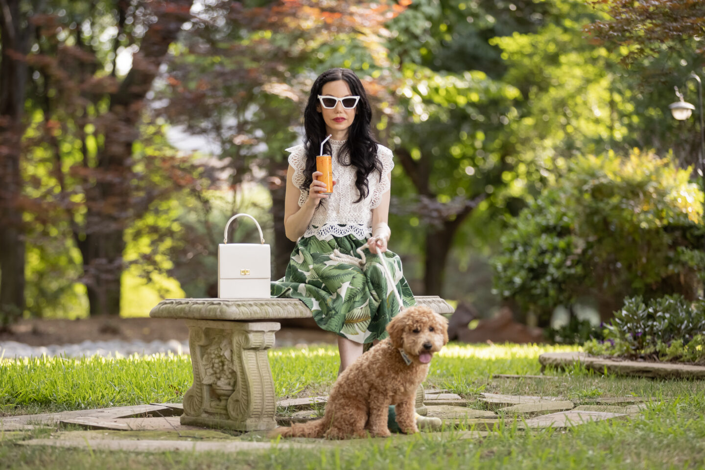 Palm Print Skirt, Neely & Chloe Bag, White Lace Top, Pink Pumps, Fashion Blogger, Fall Transitional Style, Mini Goldendoodle puppy, Fashion Blogger, Presto Sparkling Cuvee | Palm Print Skirt by popular Dallas fashion blog, Pretty Little Shoppers: image of a woman sitting outside with her dog and wearing a palm print skirt, lace cropped top, and pink heels. 