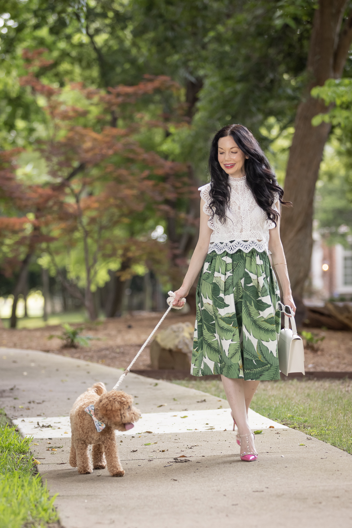 Palm Print Skirt, White Lace Top, Pink Pumps, Mini Goldendoodle Puppy | Palm Print Skirt by popular Dallas fashion blog, Pretty Little Shoppers: image of a woman walking her dog outside and wearing a palm print skirt, lace cropped top, and pink heels. 