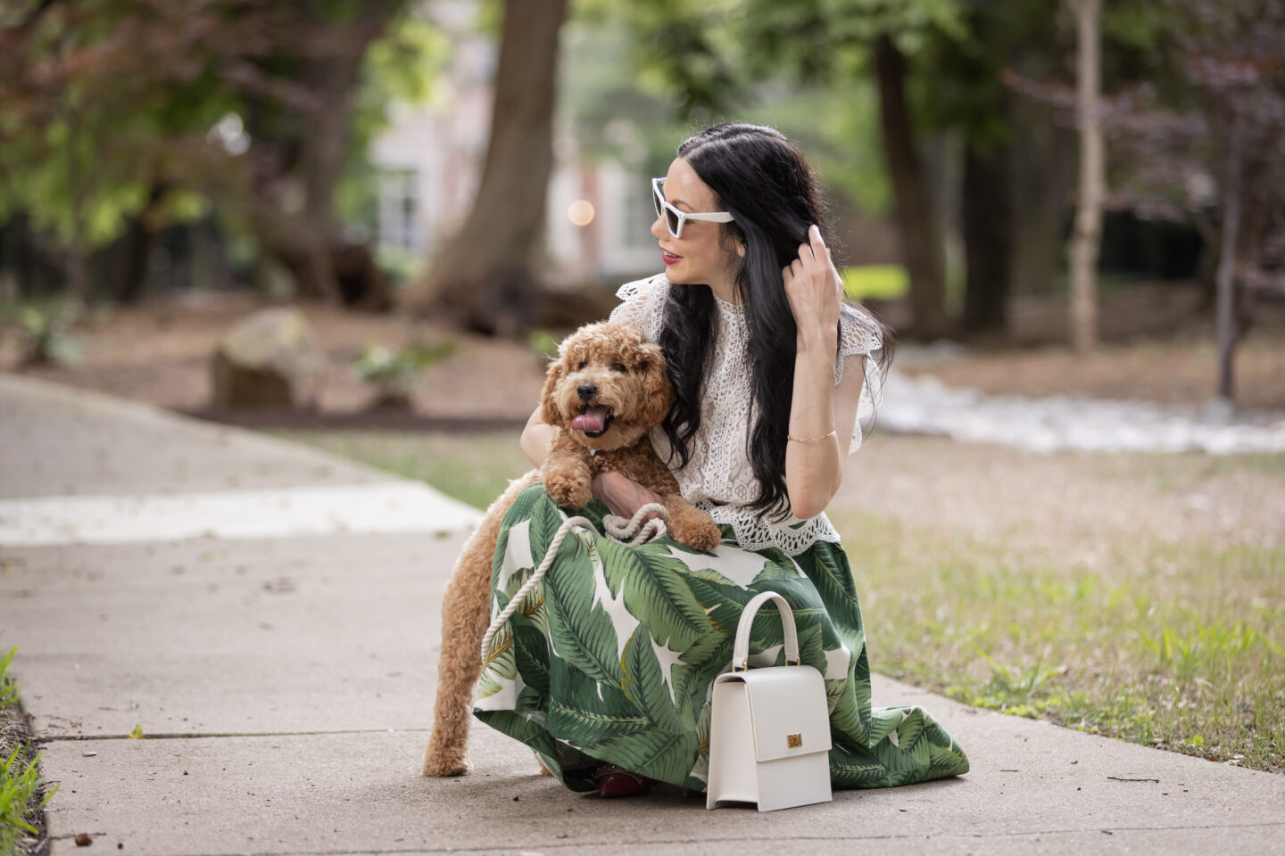 Palm Print Skirt, Neely & Chloe Bag, White Lace Top, Pink Pumps, Fashion Blogger, Fall Transitional Style, Mini Goldendoodle puppy, Fashion Blogger | Palm Print Skirt by popular Dallas fashion blog, Pretty Little Shoppers: image of a woman walking her dog outside and wearing a palm print skirt, lace cropped top, and pink heels. 