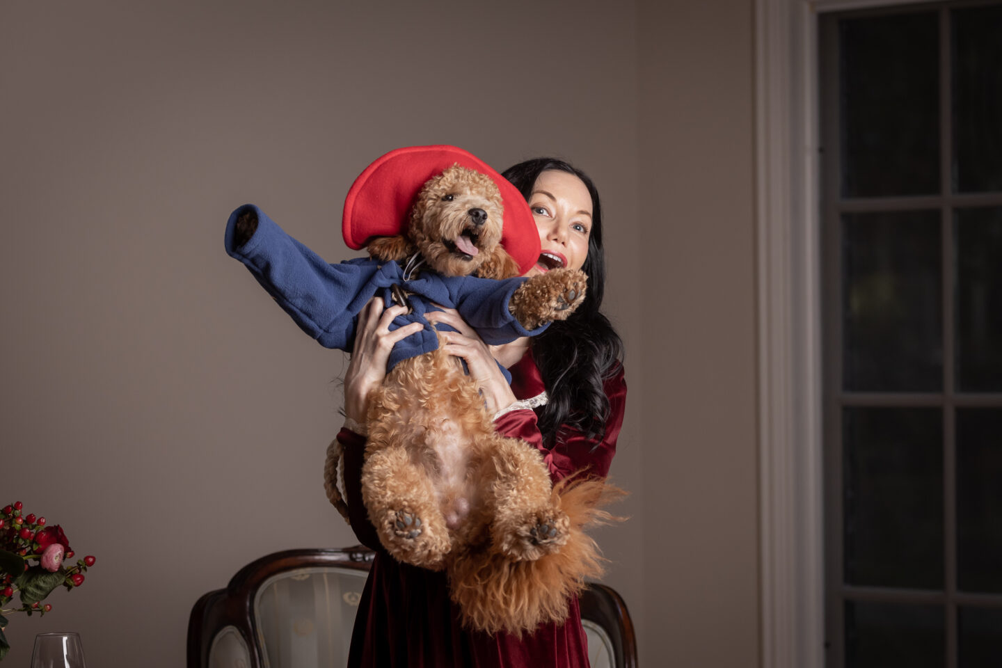 Dog in Blue Coat and Red Hat being held high in the air with out stretched arms